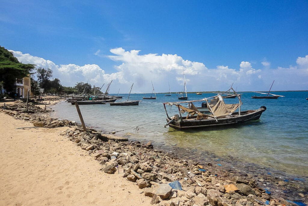 Top 7 Unique Travel Destinations to Visit in 2025 Kenya's Lamu Island, with traditional wooden dhow sailboats floating on transparent water along a rocky coastline